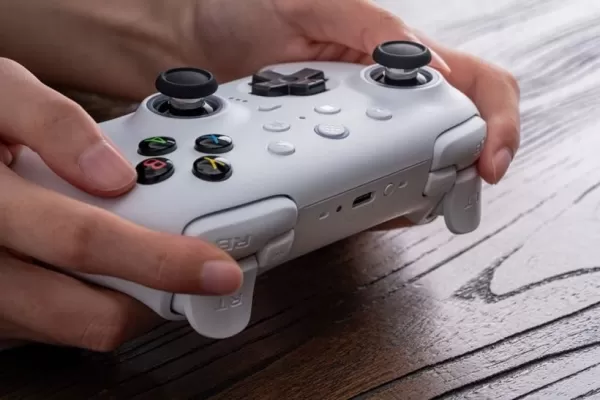 သစ်သားစားပွဲပေါ်မှာအဖြူရောင်ဂိမ်း controller ကိုင်ထားသူတစ် ဦး ၏ရုပ်ပုံ